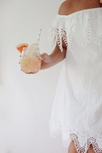 Monika wearing a white dress and holding a glass of grapefruit juice