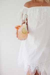 Monika wearing a white dress and holding a glass of grapefruit juice