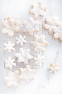 small and large snowflake cookies with icing sugar on marble counter