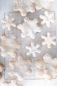 different sized snowflake cookies on cooling rack dusted with icing sugar