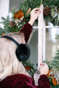 hanging wreath outside tying bow with faux fur pom pom's