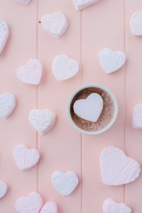 hot chocolate in mug with heart shaped marshmallows on pink board