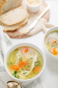 two bowls of chicken noodle soup with bread on cutting board