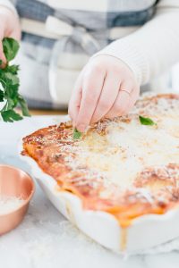 hands placing basil on lasagna