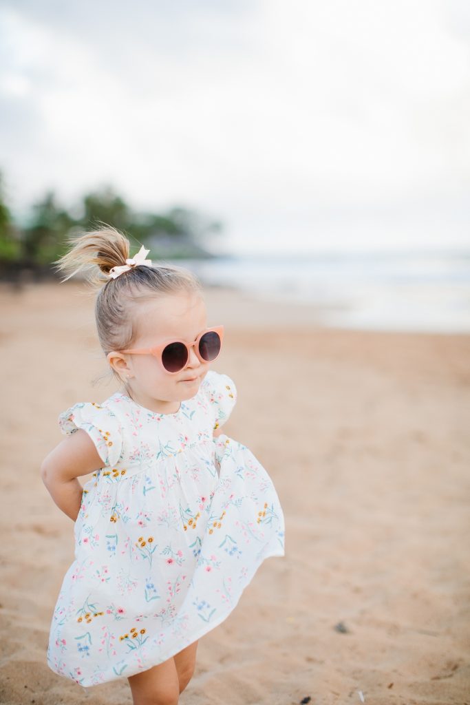little girl on beach in dress, sunglasses and hair in bow