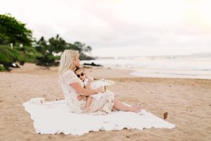 mom cuddling with little girl on beach at sunset