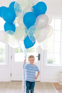 little boy holding blue and white balloons