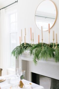 White and Pink candles on a green garland as fireplace decor with a round mirror