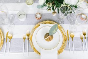 Top view of golden pair on top of gold trimmed white plates with matching utensils and glasses and white flower