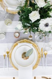 Top view of golden pear on top of gold trimmed white plates with matching utensils and glasses and white flower