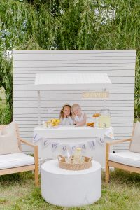 two young girls behind a lemonade booth with chairs and tables in front