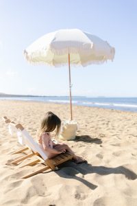 small girl sitting on a beach chair next to a beach umbrella on a beach