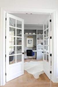 white entrance to a home office space with a grey shelving wall unit and desk and blue chair