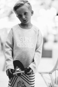 young boy with skateboard longboard and sun kissed crew neck sweater