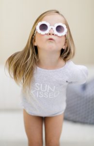 Young girl puckering lips wearing a sun kissed crew neck sweater and floral sunglasses
