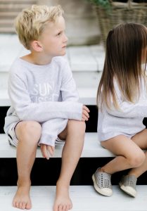young blonde boy sitting with sister on porch wearing matching crew neck sun kissed sweaters