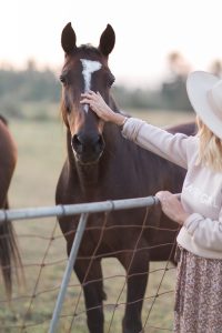 blonde woman wearing country girl sweater petting a horse