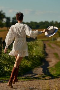 Girl in a white dress and boots holding a hat